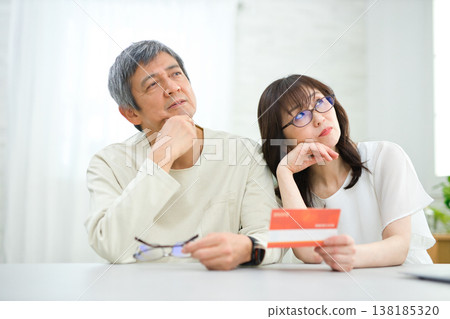A couple in their 60s looking at their savings passbook in the living room A couple in their 60s looking at their savings passbook in the living room 138185320