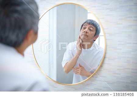 一位六十多歲的男子對著鏡子，用手撫摸自己的臉。 138185408