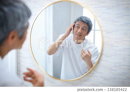 A man in his 60s looks in the mirror and worries about his gray hair. 138185422