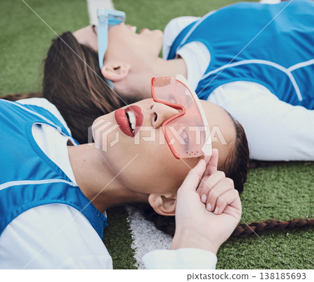 Style, sports and women hockey players relaxing on the grass field with cool, stylish and trendy outfit. Fashion, fitness and portrait of female athlete friends laying in stadium after game or match. 138185693