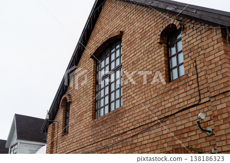Brick gable front with sizable window and visible cables against cloudy sky environment Brick gable front with sizable window and visible cables against cloudy sky environment 138186323