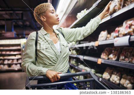 Grocery, shopping cart and woman in supermarket at shelf for food at retail convenience store. Groceries, serious and African customer on trolley at shop to check product price, sales choice and cost Grocery, shopping cart and woman in supermarket at shelf for food at retail convenience store. Groceries, serious and African customer on trolley at shop to check product price, sales choice and cost 138186363