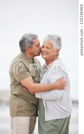 Senior couple, kiss or hug on beach with smile, embrace and enjoying for retirement, happy or love. Senior citizen, romance and lovers with bond, happiness and vacation for travel, anniversary or fun 138186968
