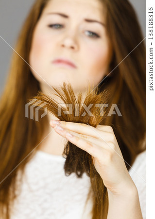 Worried woman looking at her dry hair ends Worried woman looking at her dry hair ends 138188316