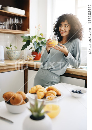 Woman, smile and thinking with orange juice in kitchen for breakfast, nutrition and vitamin c in the morning. Food, person and happiness with idea and drink with pajamas or natural face for wellness 138188422