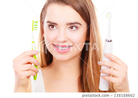 Woman with braces holding electric and traditional toothbrush Woman with braces holding electric and traditional toothbrush 138188602