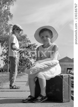 Children in vintage clothing waiting at a train station with luggage and a toy Children in vintage clothing waiting at a train station with luggage and a toy 138188767