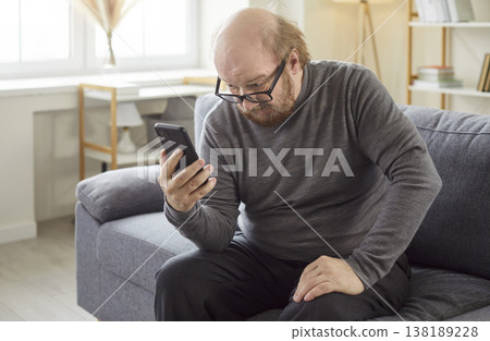 Indoor shot of serious bearded senior man in eyewear focused in smartphone screen checking email box Indoor shot of serious bearded senior man in eyewear focused in smartphone screen checking email box 138189228