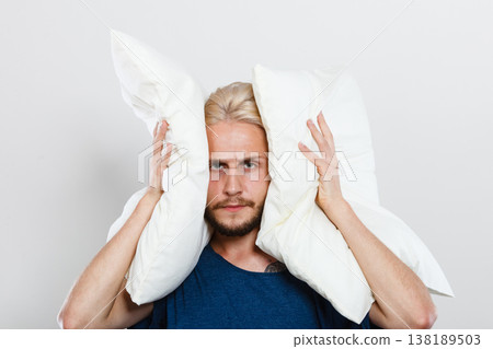 Sad man closing ears with pillows 138189503