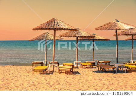 Tropical beach scenery with sun parasols and evening sky. Straw sun umbrellas on the beach Tropical beach scenery with sun parasols and evening sky. Straw sun umbrellas on the beach 138189864