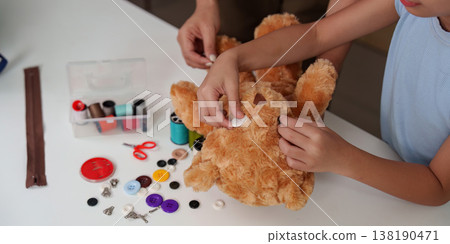 Child repairing a teddy bear with sewing tools 138190471