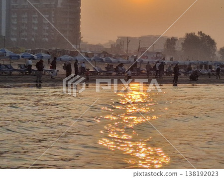 Golden Sunset Over a Bustling Beach with Relaxing Visitors 138192023