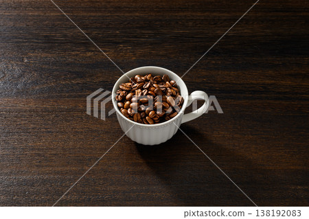 Coffee beans in a white cup against a wood grain background Coffee beans in a white cup against a wood grain background 138192083