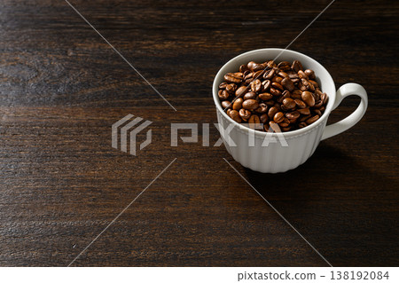 Coffee beans in a white cup against a wood grain background Coffee beans in a white cup against a wood grain background 138192084
