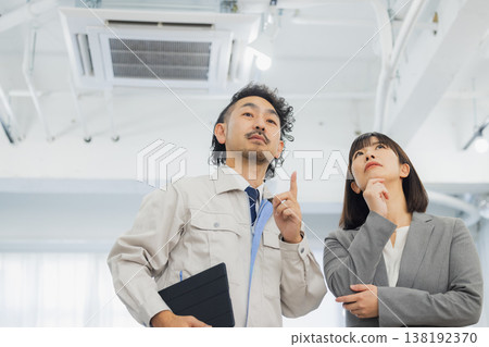 A businesswoman and a worker with dissatisfied expressions looking at the air conditioner 138192370