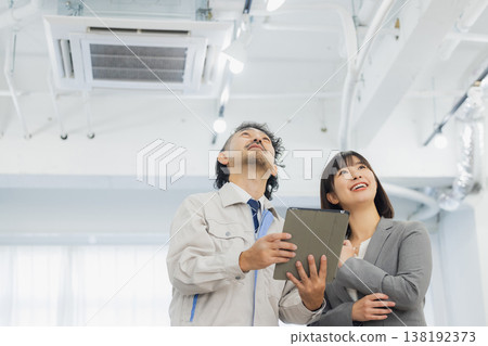 一位女商人和一個工人面露不滿地看著空調。 一位女商人和一個工人面露不滿地看著空調。 138192373