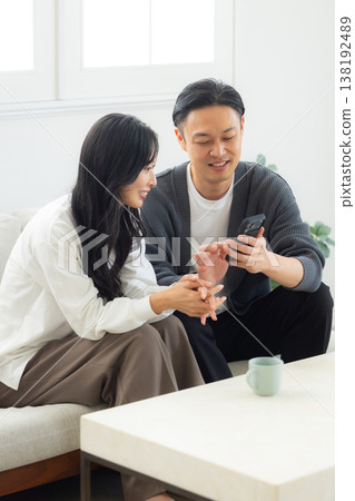 一對情侶坐在沙發上看著他們的智慧型手機 一對情侶坐在沙發上看著他們的智慧型手機 138192489