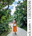 一名身穿橘色洋裝的女子走過沖繩一條綠色的隧道公路。 138192696