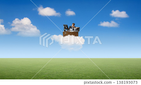 Businessman working at desk on cloud above field under blue sky. Businessman working at desk on cloud above field under blue sky. 138193073