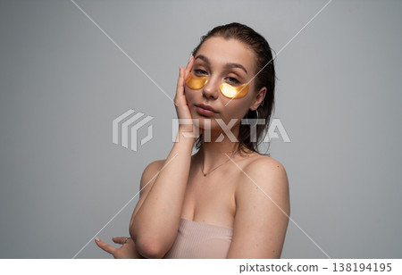 Young woman applying gold eye patches to her under-eye area, focusing on beauty, hydration, and a relaxing self-care routine for glowing, healthy skin 138194195