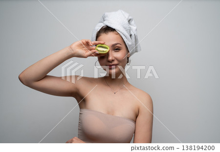 Young woman showcasing natural beauty and healthy skin concepts, holding a halved kiwi fruit over one eye after a shower, ready for a skincare routine Young woman showcasing natural beauty and healthy skin concepts, holding a halved kiwi fruit over one eye after a shower, ready for a skincare routine 138194200