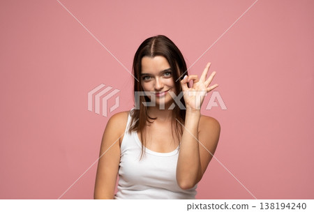 Young brunette woman making an ok gesture, expressing agreement, satisfaction, and success with a friendly smile 138194240