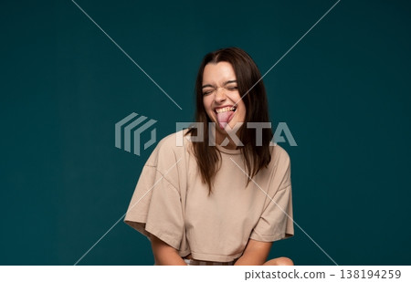 Playful young woman making a funny face, sticking tongue out and grimacing with closed eyes, expressing humor and mischief Playful young woman making a funny face, sticking tongue out and grimacing with closed eyes, expressing humor and mischief 138194259