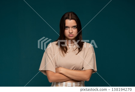 Young woman expressing defiance with crossed arms and a serious facial expression on a plain background Young woman expressing defiance with crossed arms and a serious facial expression on a plain background 138194270