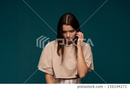 Young woman feeling pensive and concerned, touching her ear while looking down with a sad expression Young woman feeling pensive and concerned, touching her ear while looking down with a sad expression 138194271