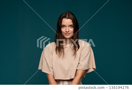 Smiling young woman posing with confidence against a turquoise background, feeling happy and casual 138194276