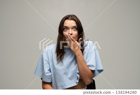 Young woman covering mouth with hand expressing shock and surprise, feeling disbelief or amazed by unexpected news 138194280