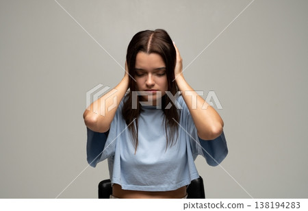 Young woman feeling overwhelming noise and pain, eyes closed, covering ears to block out sound and minimize distraction 138194283