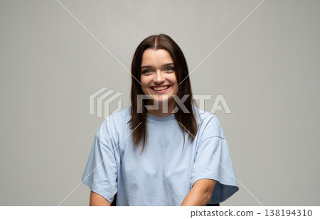 Young smiling woman posing in light blue t-shirt feeling happy and positive looking at camera in studio Young smiling woman posing in light blue t-shirt feeling happy and positive looking at camera in studio 138194310