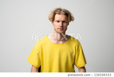 Young blond man with messy hair and yellow t-shirt making a silly cross-eyed facial expression, showing playful mood and humor on a studio background Young blond man with messy hair and yellow t-shirt making a silly cross-eyed facial expression, showing playful mood and humor on a studio background 138194333