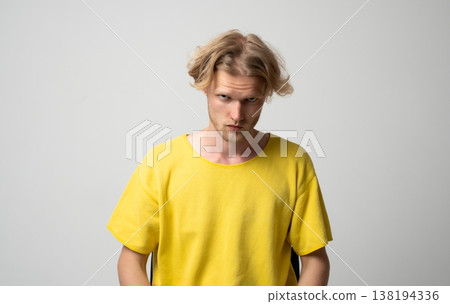 Young man with an intense glare looking straight at the camera, portraying feelings of anger, frustration, and aggression while wearing a casual yellow t-shirt against a plain background Young man with an intense glare looking straight at the camera, portraying feelings of anger, frustration, and aggression while wearing a casual yellow t-shirt against a plain background 138194336