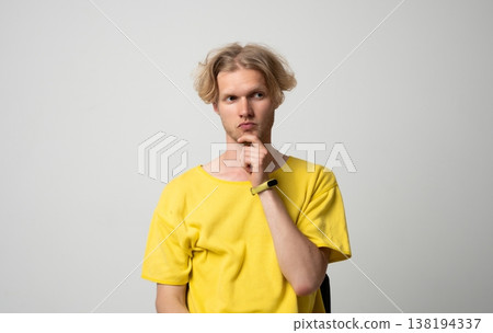 Young man with blond hair in yellow t-shirt pondering a solution. Contemplating complex ideas. Feeling confused and in doubt about making a decision 138194337