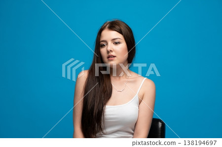 Young woman feeling anxious and uncertain, looking away with worried expression on blue background Young woman feeling anxious and uncertain, looking away with worried expression on blue background 138194697