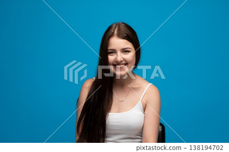Young woman smiling with broad happiness against a vibrant blue background, expressing joy and positive emotions 138194702