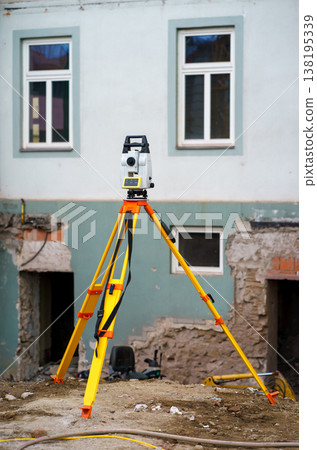 Geodetic surveying instrument on tripod at construction site, used for measurement and planning during building renovation and engineering work. Geodetic surveying instrument on tripod at construction site, used for measurement and planning during building renovation and engineering work. 138195339
