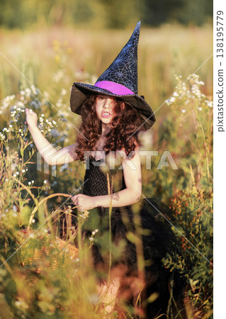 A girl in a black dress and a witch's hat collects herbs for a potion. A girl in a black dress and a witch's hat collects herbs for a potion. 138195779