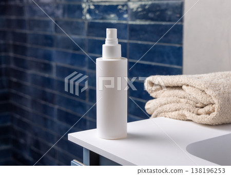 White spray cosmetic bottle near white bath towel in dark blue bathroom, cosmetic mockup White spray cosmetic bottle near white bath towel in dark blue bathroom, cosmetic mockup 138196253