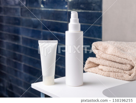White bottle and tube near beige bath towel in blue bathroom, cosmetic packaging mockup White bottle and tube near beige bath towel in blue bathroom, cosmetic packaging mockup 138196255