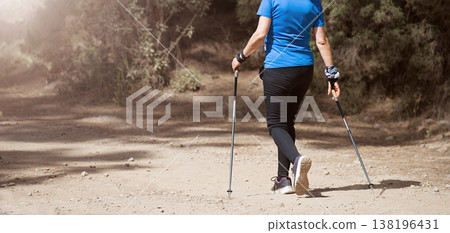 Senior woman walking in forest with Nordic walking sticks, sunny summer day. An active lifestyle in retirement, a hike in nature Senior woman walking in forest with Nordic walking sticks, sunny summer day. An active lifestyle in retirement, a hike in nature 138196431