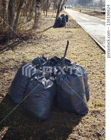 Garbage bags piled near a walking path in a park on a sunny day in springtime Garbage bags piled near a walking path in a park on a sunny day in springtime 138196624