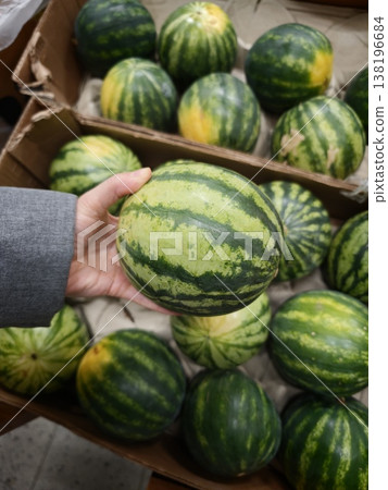 Watermelons are displayed in a market with a hand holding one of the fruits Watermelons are displayed in a market with a hand holding one of the fruits 138196684
