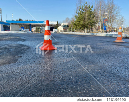 Traffic cones placed on a wet asphalt surface near a gas station on a sunny day 138196690