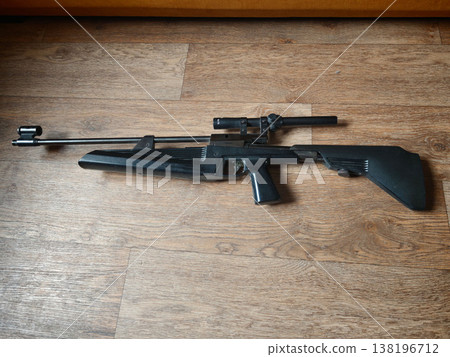 Black rifle displayed on wooden floor in indoor setting during daytime Black rifle displayed on wooden floor in indoor setting during daytime 138196712