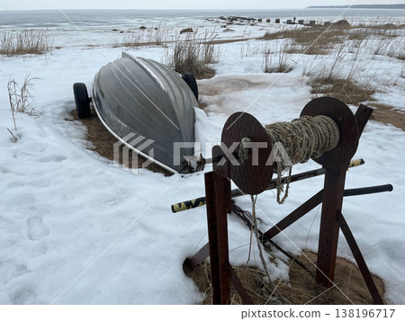 Winter scene shows a boat on snow-covered shore near frozen water at low tide 138196717