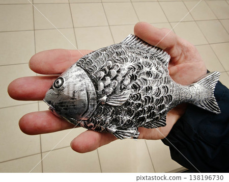 Person holds a silver fish sculpture in their hand in a store setting Person holds a silver fish sculpture in their hand in a store setting 138196730