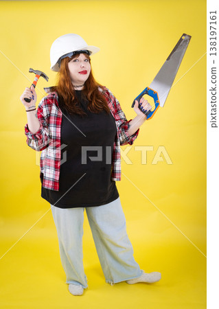 Woman wearing hard hat holding hammer and saw 138197161